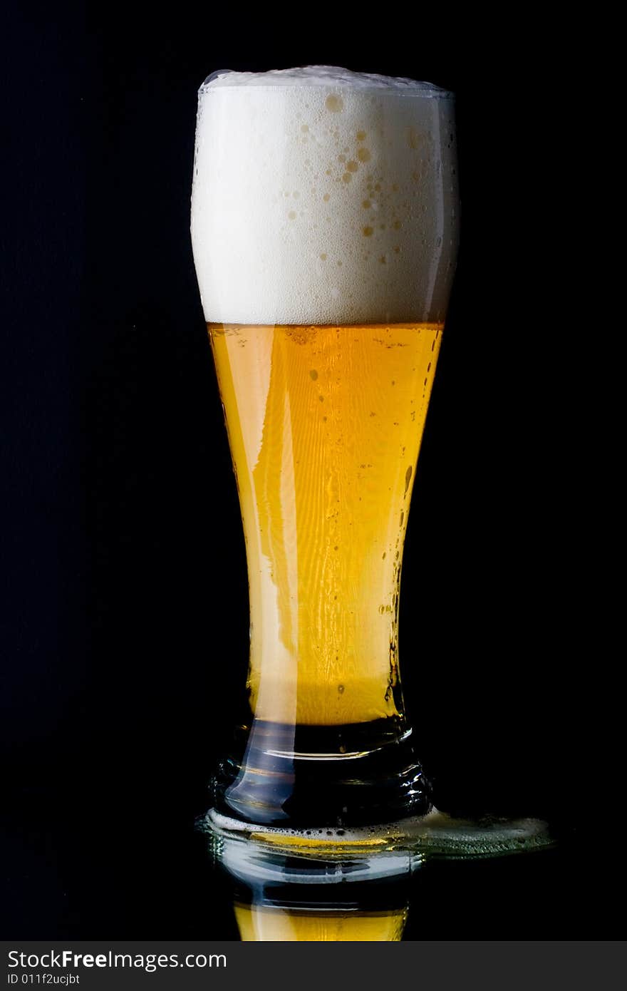 Fresh foamy beer in a glass on a black background.