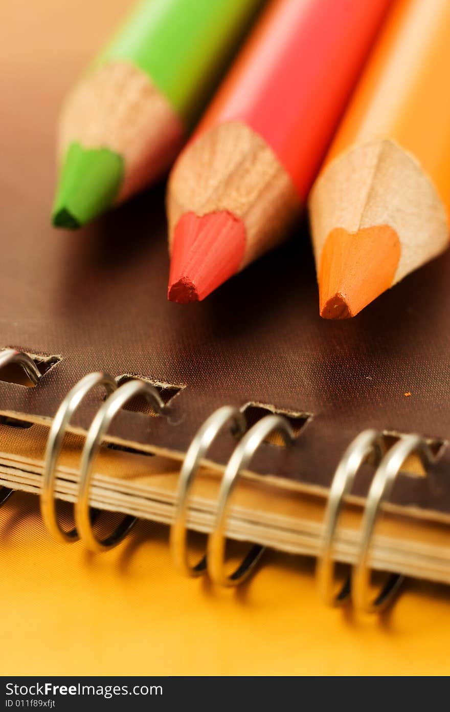 Bright and colorful coloring pencils, green, red and orange on notebook - closeup. Bright and colorful coloring pencils, green, red and orange on notebook - closeup