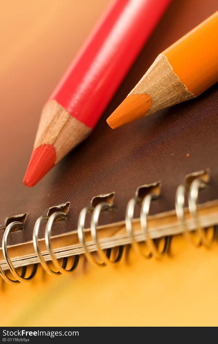 Bright and colorful coloring pencils, red and orange on notebook - closeup. Bright and colorful coloring pencils, red and orange on notebook - closeup