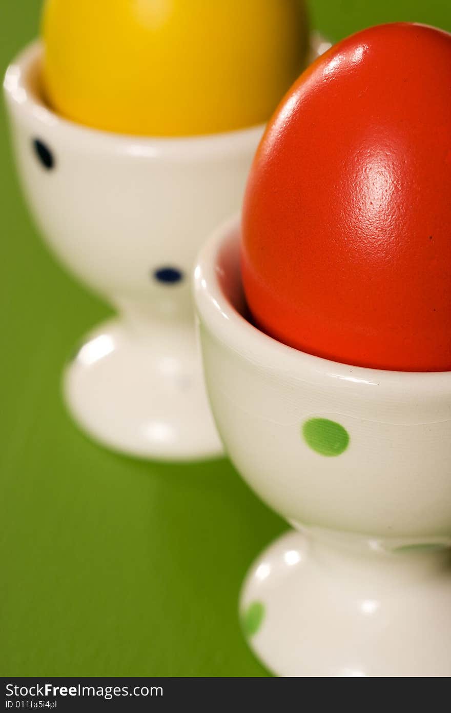 Yellow and red Easter Eggs in white bowl on green background