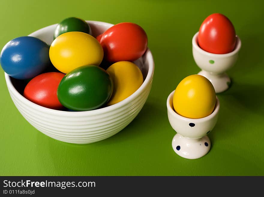 Colorful Easter Eggs in white bowl on green background