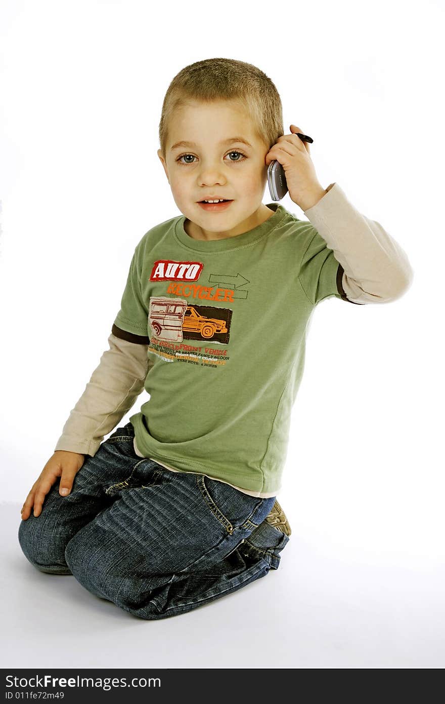 Young boy in a green T-shirt kneeling pretending to be talking on a cell phone. Young boy in a green T-shirt kneeling pretending to be talking on a cell phone