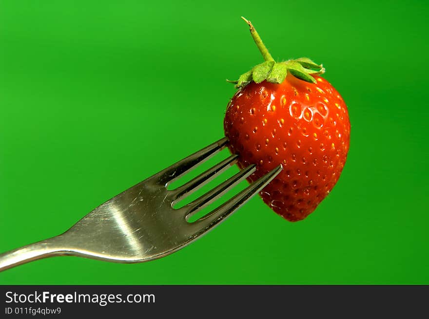 One strawberry on fork on green background. One strawberry on fork on green background