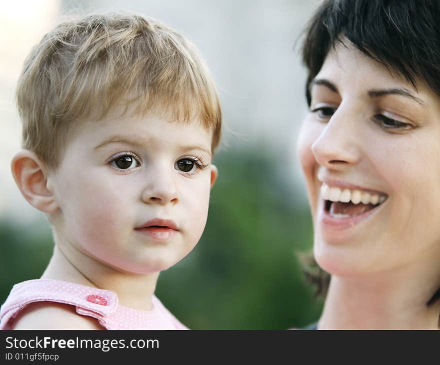 Sweet baby girl in the arms of a happy smiling mother outdoors. Sweet baby girl in the arms of a happy smiling mother outdoors