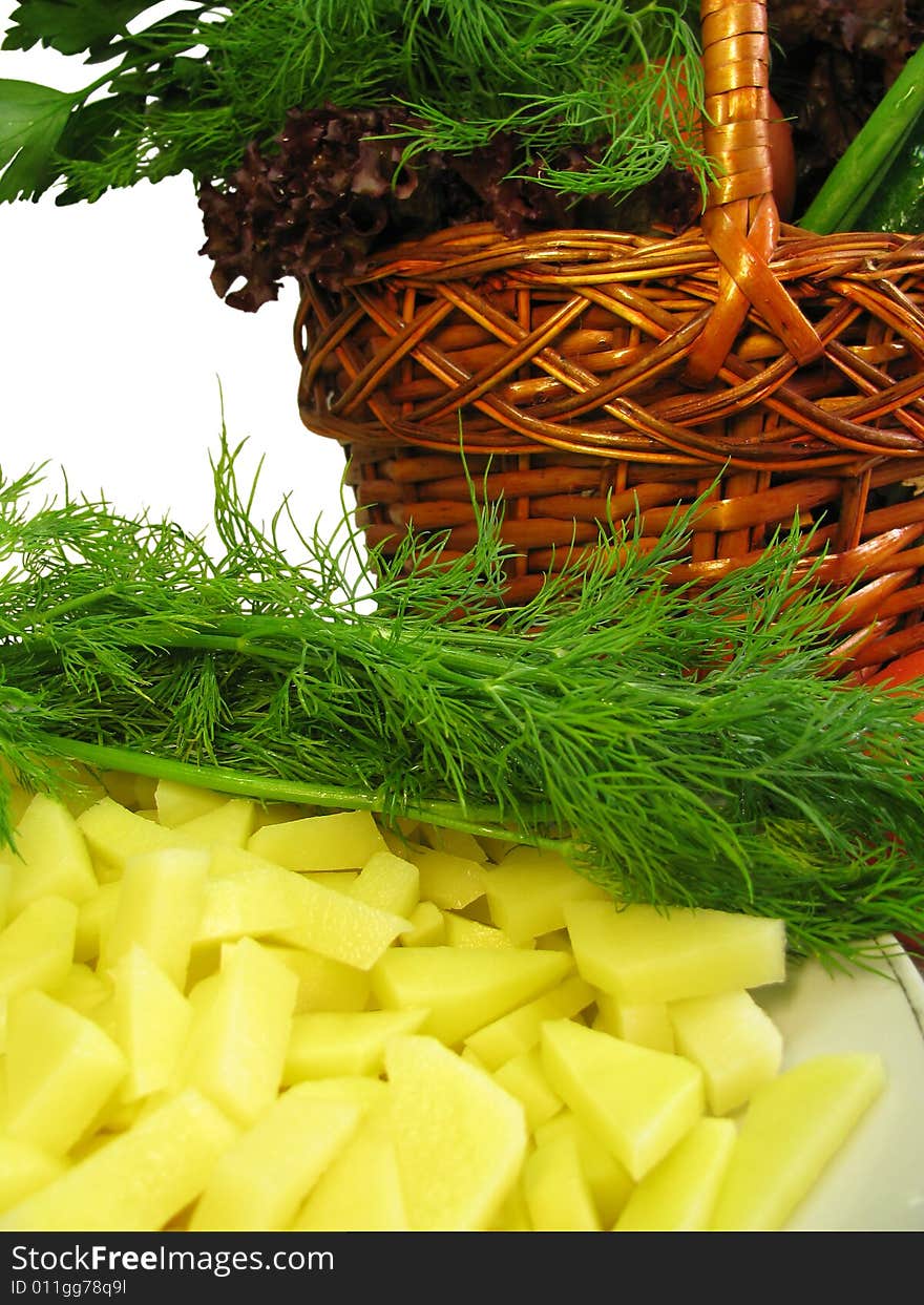 Vegetables placed in wicker basket and a plate with cut potatoes. Vegetables placed in wicker basket and a plate with cut potatoes