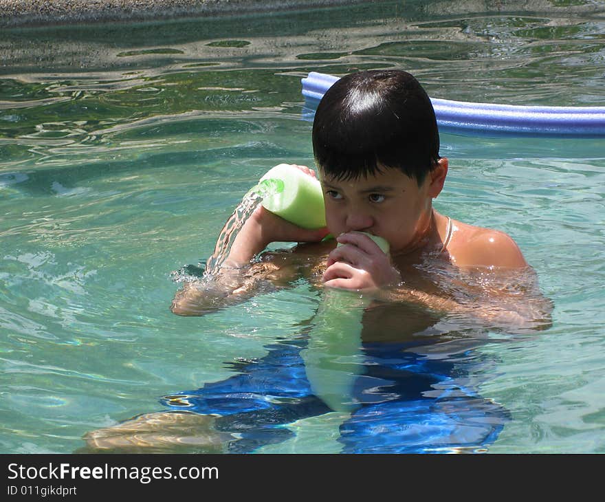 Dark haired boy in swimming pool shooting water through a pool toy. Dark haired boy in swimming pool shooting water through a pool toy