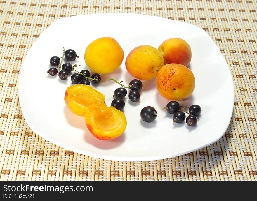 Ripe apricots and black currant on a white plate. Ripe apricots and black currant on a white plate