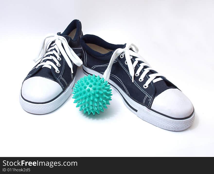 Black-and-white classical gym shoes and green ball on a white background. Black-and-white classical gym shoes and green ball on a white background