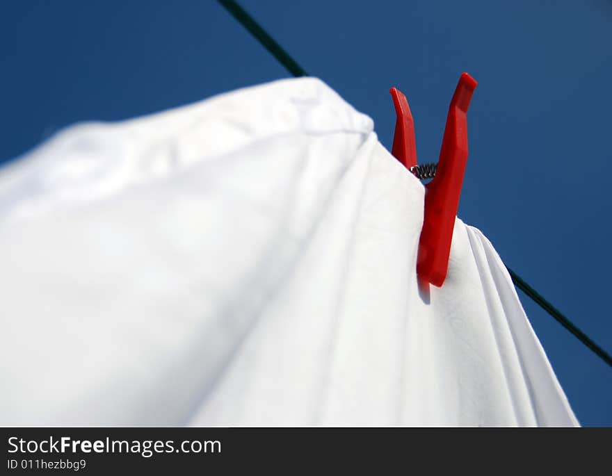 Solitary red clothes peg keeps a firm hold on white laundry, shouting: Look at me; I'm in control!