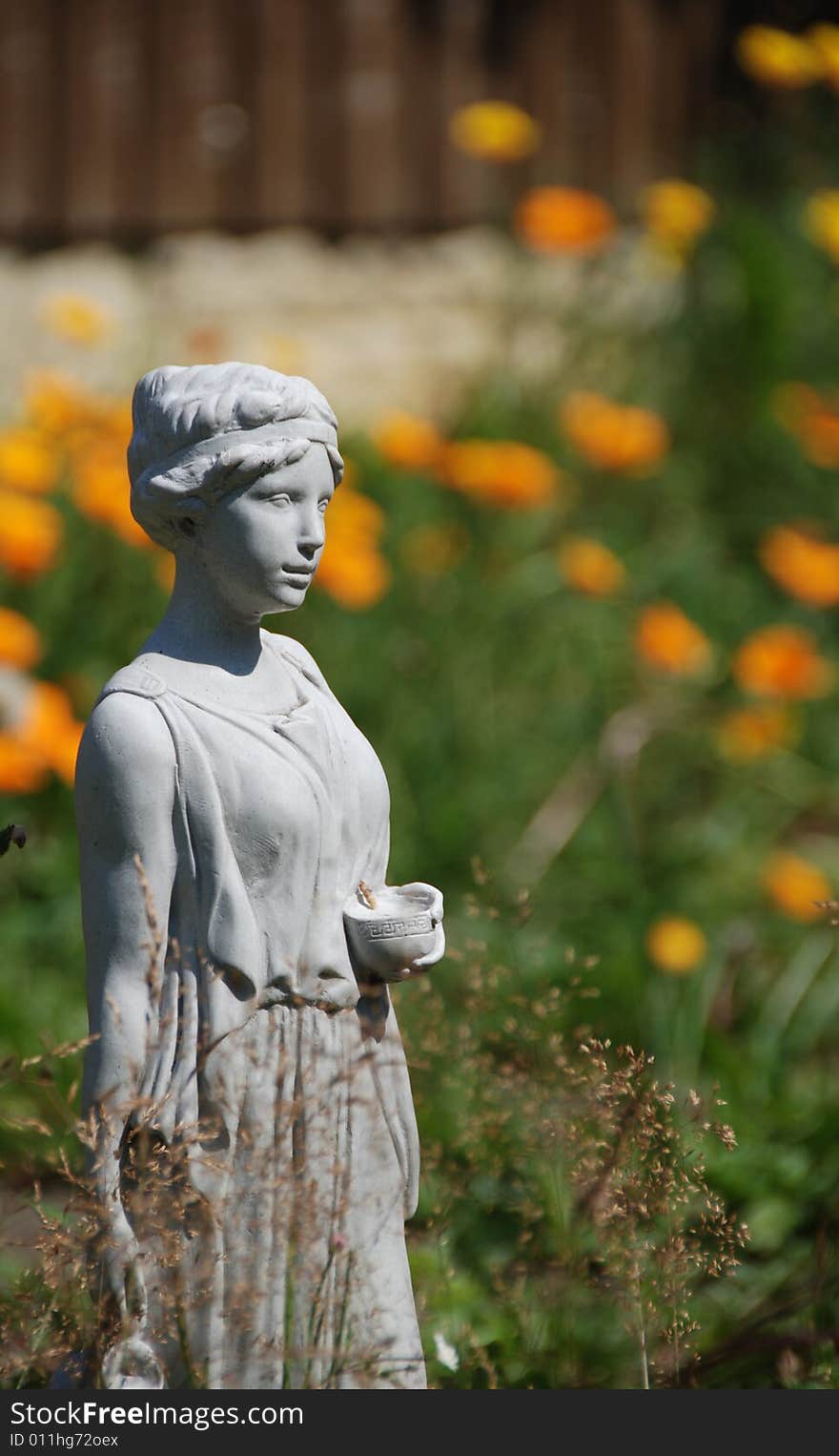 Garden statue of girl waits with a cup in her hand against an out-of-focus background of orange fllowers. Garden statue of girl waits with a cup in her hand against an out-of-focus background of orange fllowers