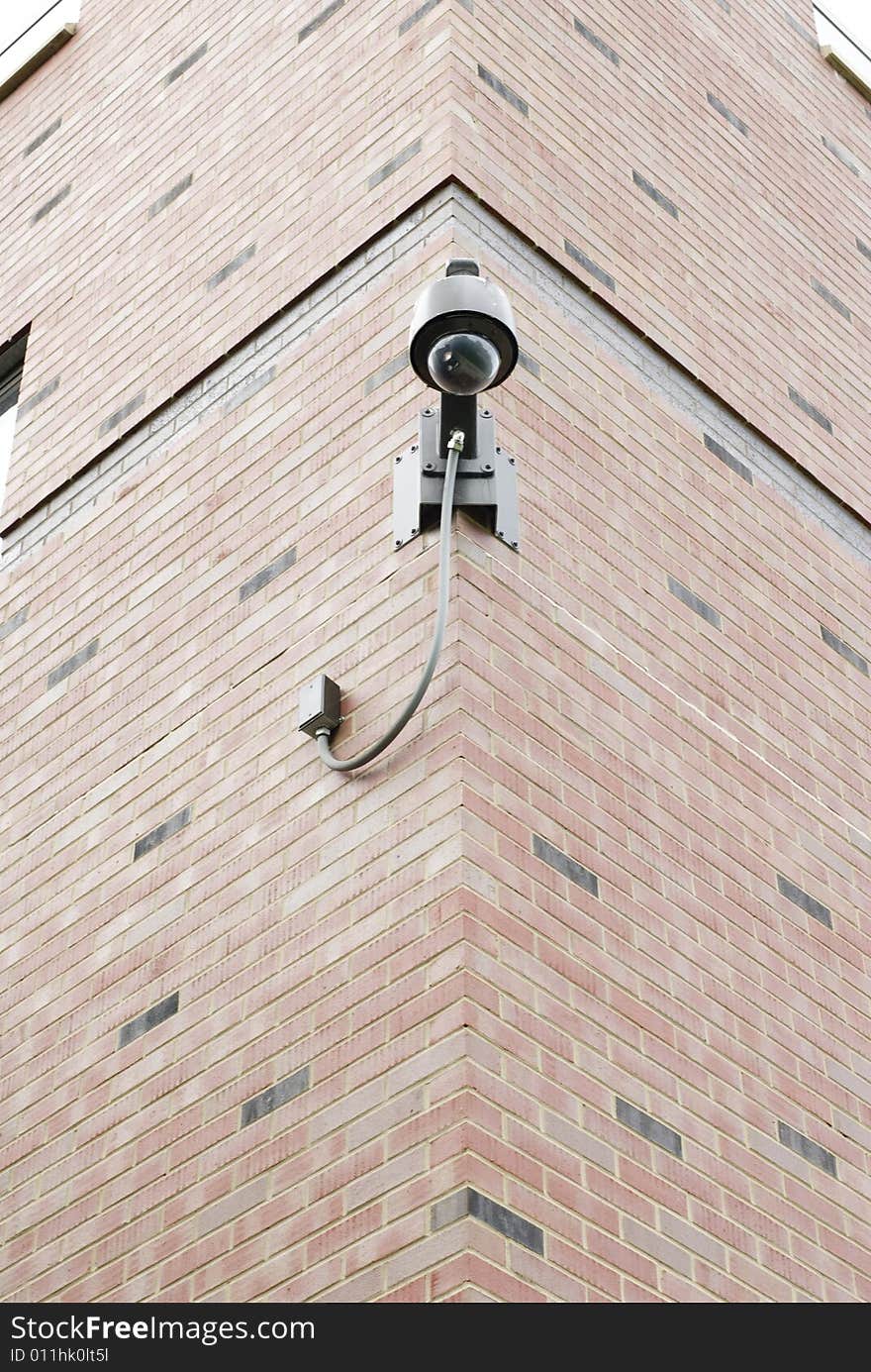 Mounted on the corner of a brick wall, a bubble-glass overhead security camera observes its surroundings. Mounted on the corner of a brick wall, a bubble-glass overhead security camera observes its surroundings.