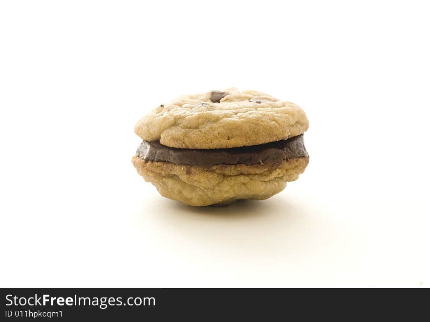 A chocolate chip cookie sandwiches with chocolate filling on a white backdrop.