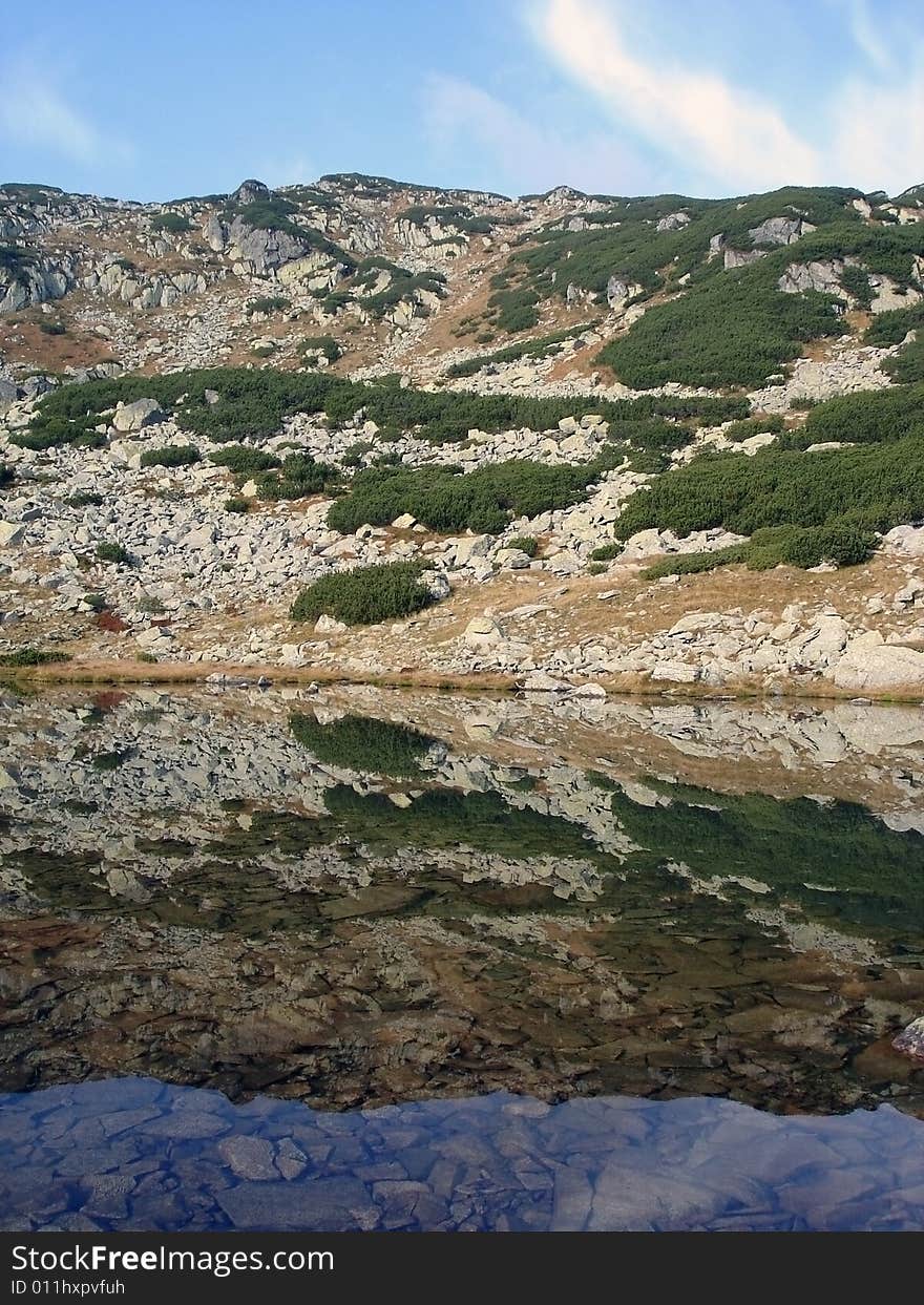 Symmetry In Nature: Reflection On The Calm Water Of A Tranquil Mountain Lake Retezat National Park. Symmetry In Nature: Reflection On The Calm Water Of A Tranquil Mountain Lake Retezat National Park.