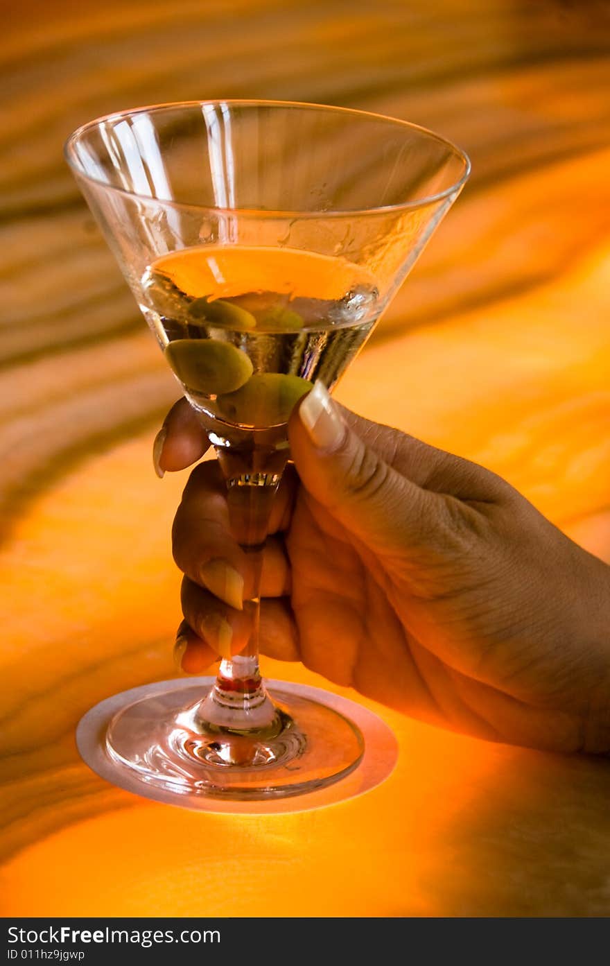 Dirty Martini with green olives, held by a woman's hand on a colorful bar countertop. Dirty Martini with green olives, held by a woman's hand on a colorful bar countertop