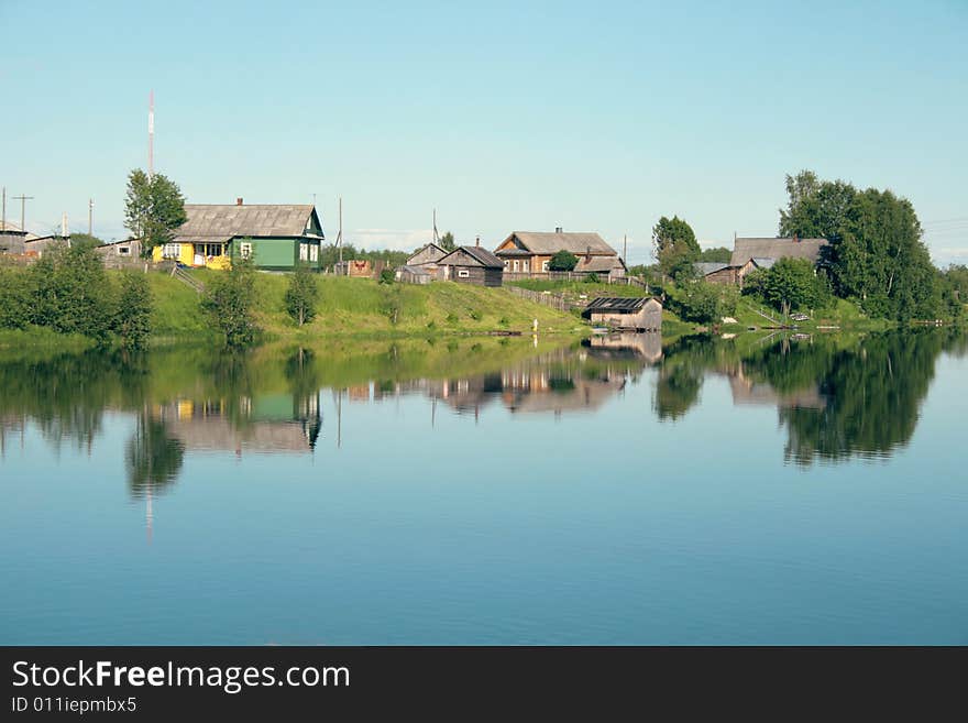 Village on the bank of the river and its reflection in the water