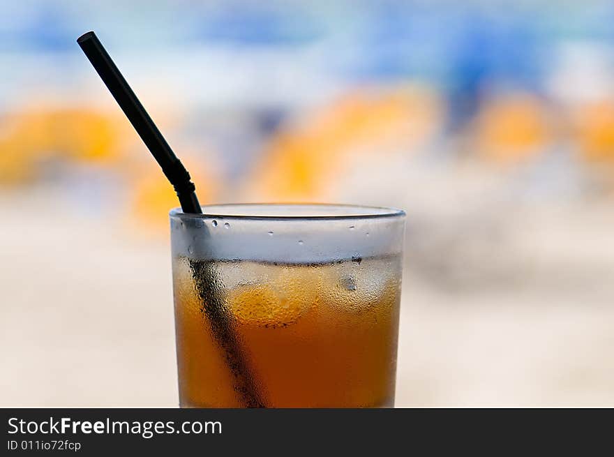 Glass of cold ice tea on table with blurred beach in background. Glass of cold ice tea on table with blurred beach in background