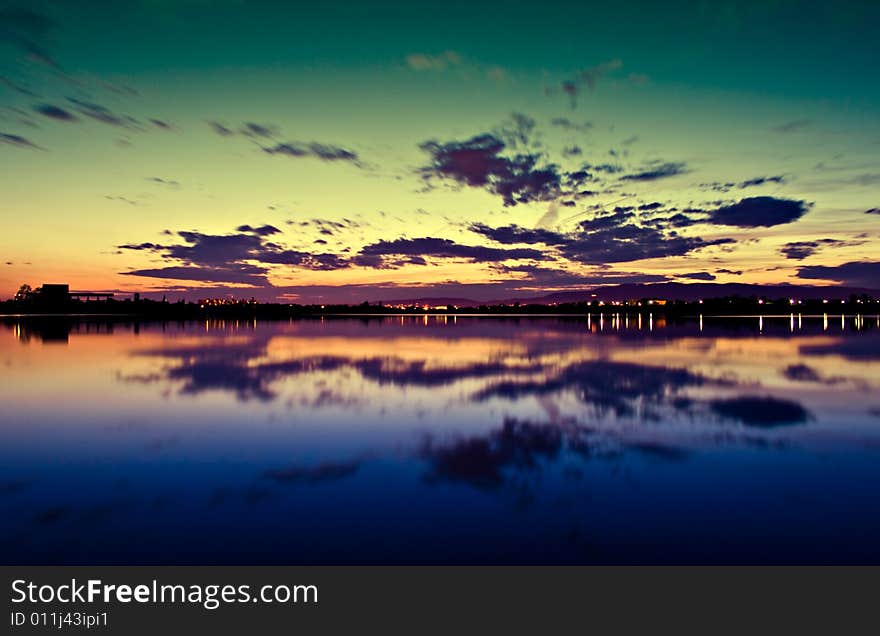 The beautiful sunset with green/orange colored clouds and reflection in the blue water