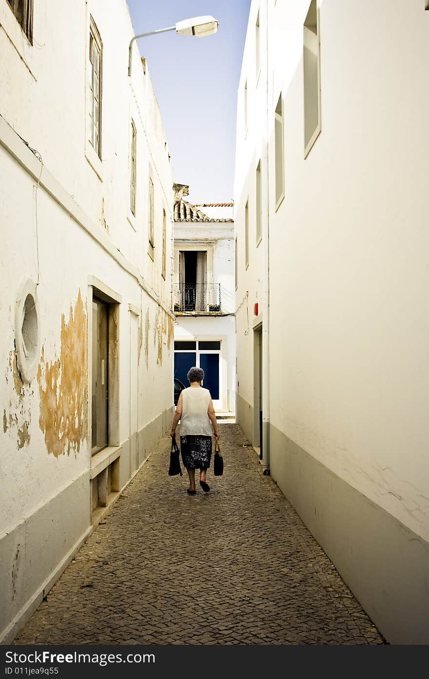 Old woman walking among old cracked white walls. Old woman walking among old cracked white walls.