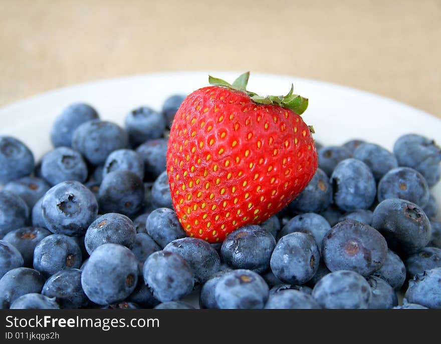 One fresh strawberry sitting on top of a group of fresh blueberries. One fresh strawberry sitting on top of a group of fresh blueberries.