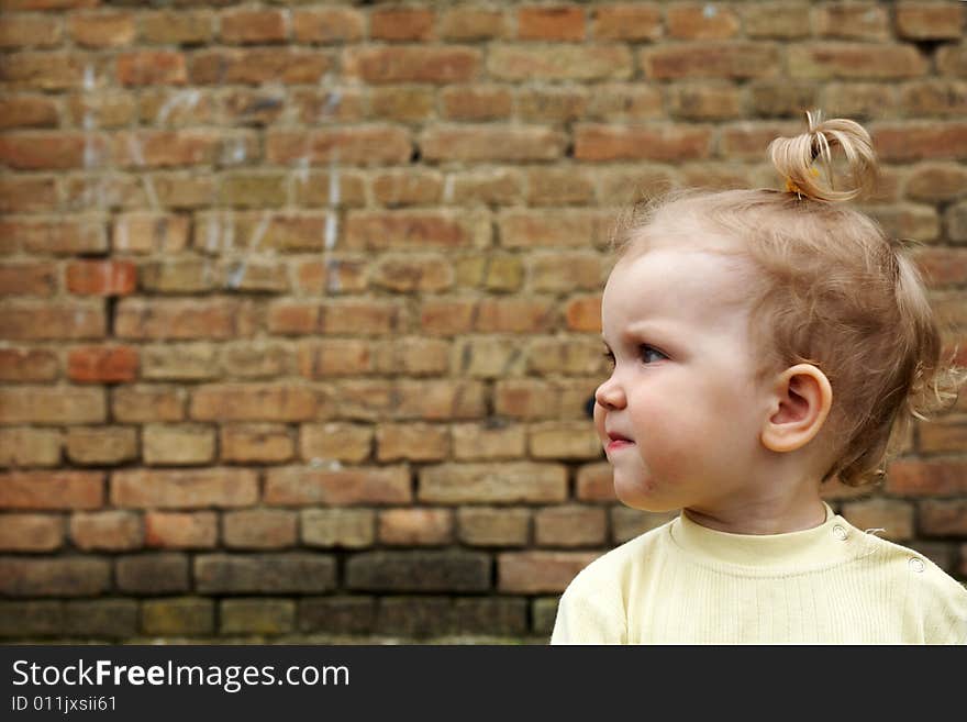 An image of baby-girl near a yellow brick wall