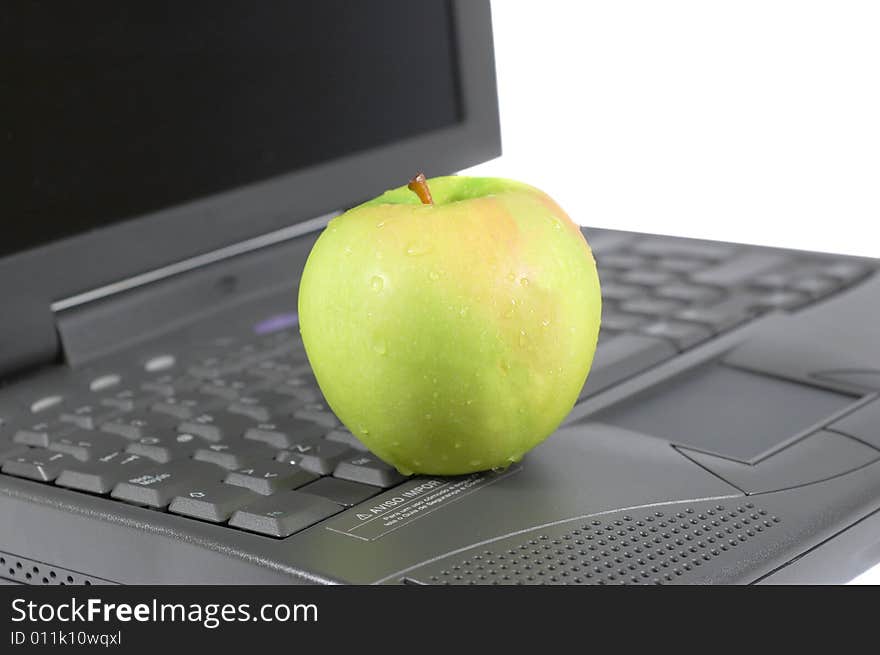 A green apple on top of a laptop. A green apple on top of a laptop