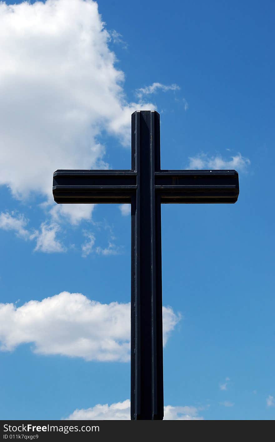 Black metal cross on a cloudy blue sky background. Black metal cross on a cloudy blue sky background