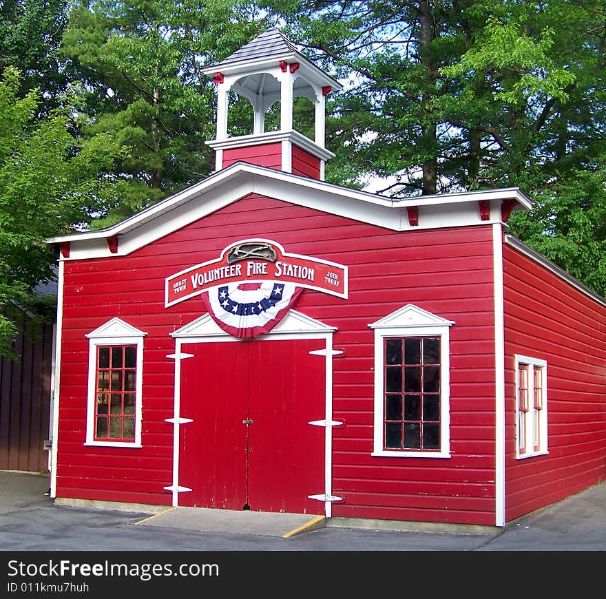A little replica of a fire station stands colored in 
bright red and white in the afternoon sunshine.