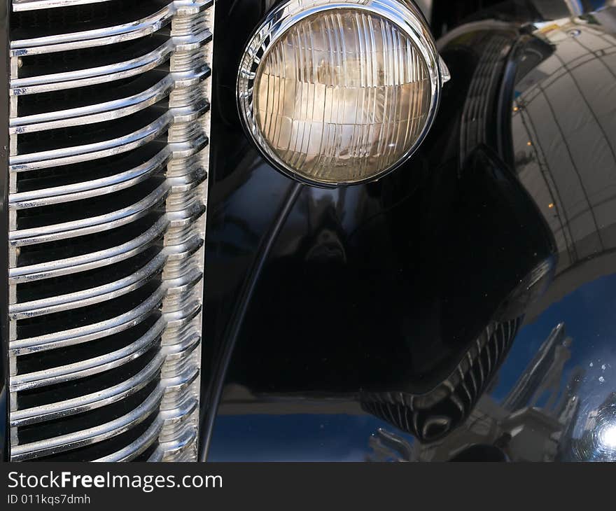 Close up of radiator grille and headlights of vintage black car with reflective shiny surface. Close up of radiator grille and headlights of vintage black car with reflective shiny surface