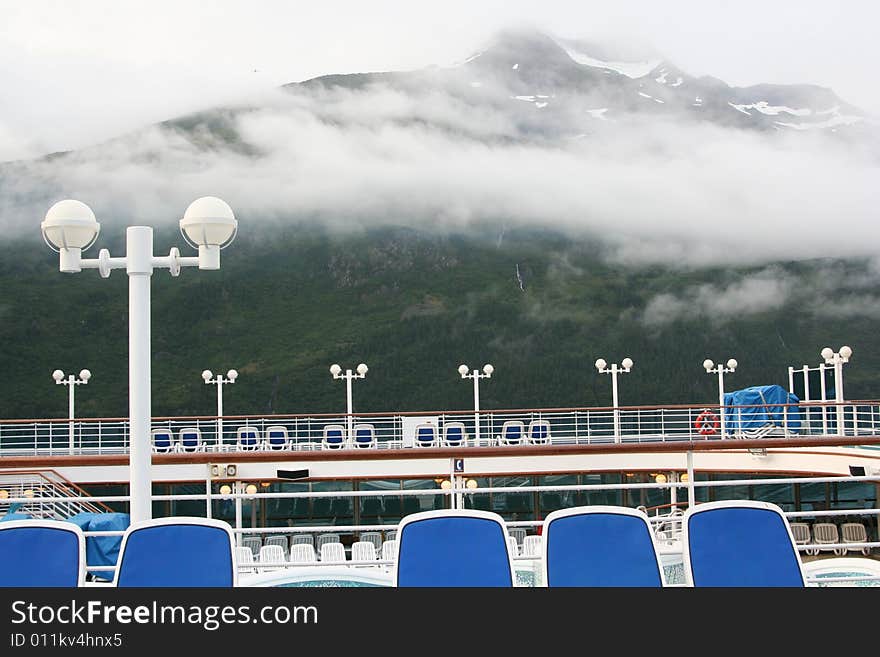 On the deck of a cruise ship in Whittier, Alaska, with low clouds and blue and white deck chairs. On the deck of a cruise ship in Whittier, Alaska, with low clouds and blue and white deck chairs.