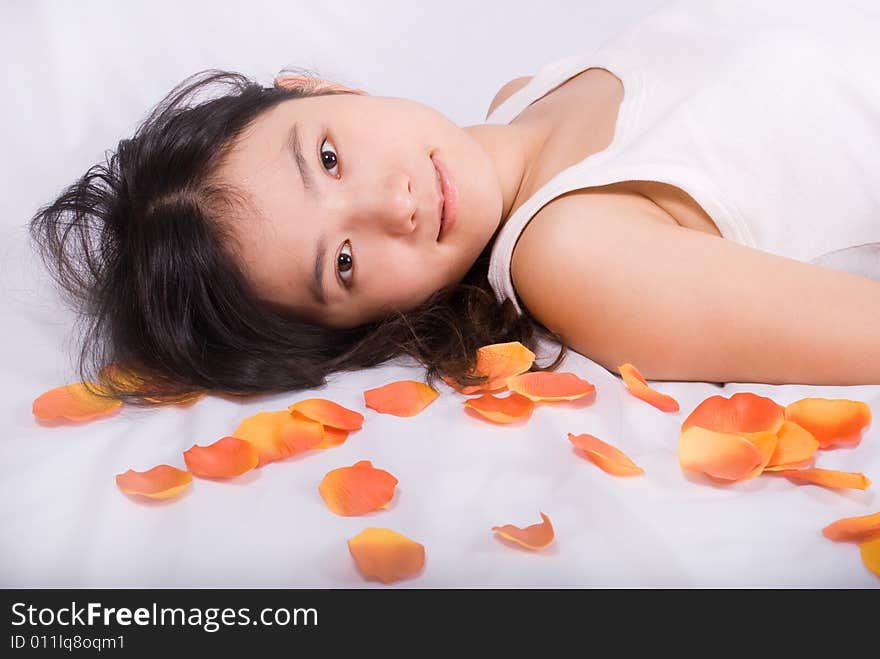 Young asian female is lying on white background with fallen orange petals. Young asian female is lying on white background with fallen orange petals