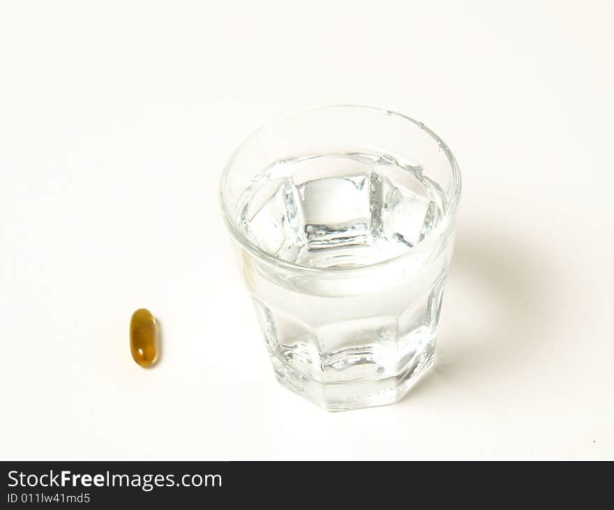 A pill ready to be taken next to a glass or water. A pill ready to be taken next to a glass or water.