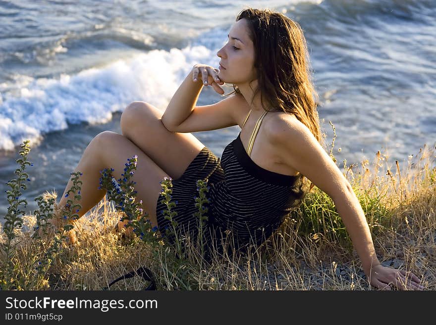 Pretty young woman sitting on the grass beside the sea. Pretty young woman sitting on the grass beside the sea