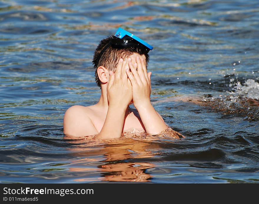 The boy is covering his face with hands in a small lake late afternoon. The boy is covering his face with hands in a small lake late afternoon.