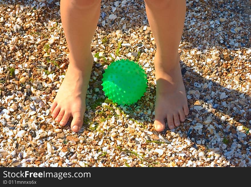 Child legs on sand with green ball