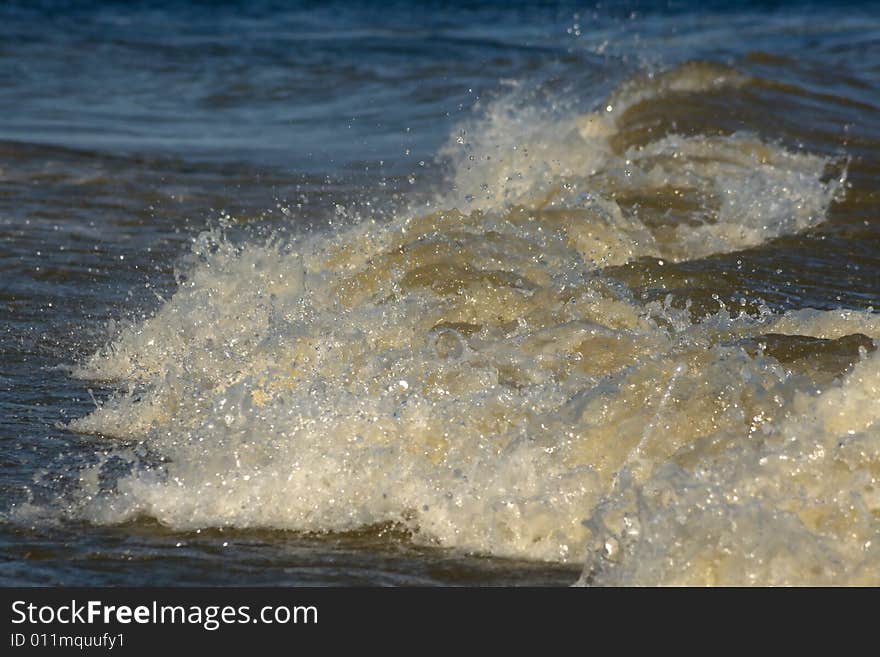 The wave falls ashore with spray and noise.