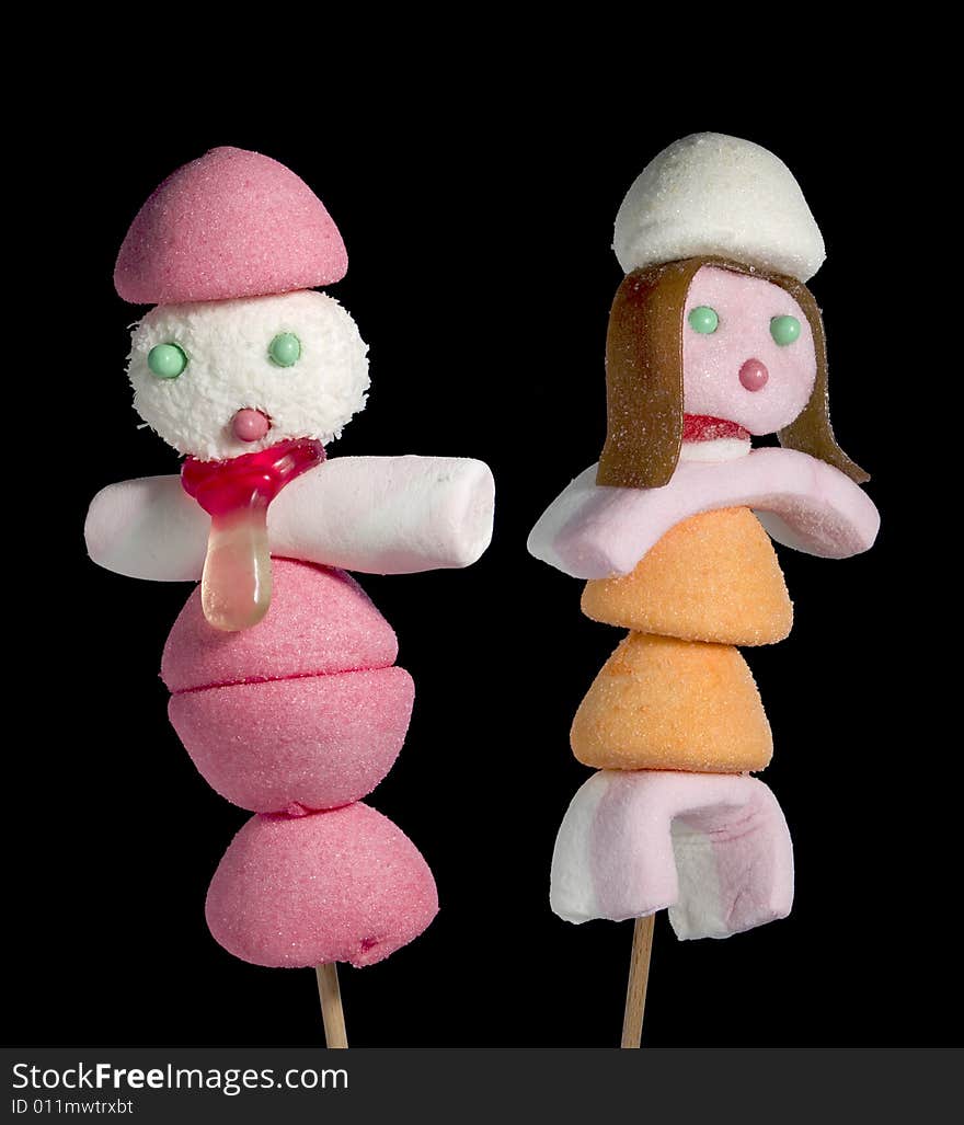 A male and a female figurine made out of candies on a stick over a black background. A male and a female figurine made out of candies on a stick over a black background.