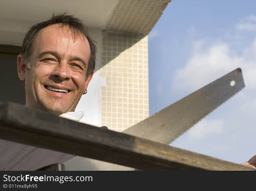 A man, stands smiling, sawing a piece of wood. Horizontally framed shot. A man, stands smiling, sawing a piece of wood. Horizontally framed shot.