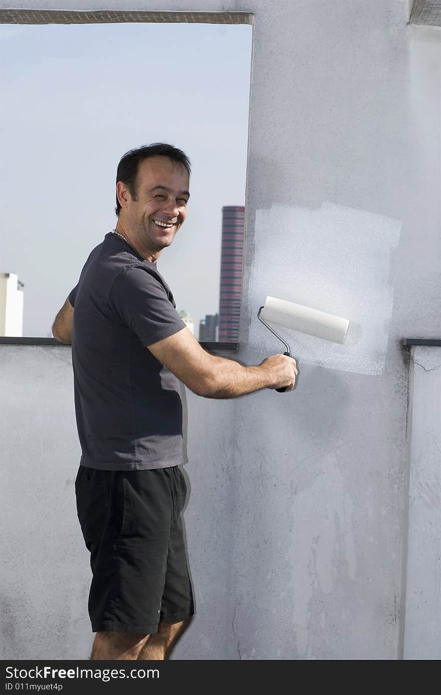 Attractive man smiling and painting wall with roller. Vertically framed shot. Attractive man smiling and painting wall with roller. Vertically framed shot