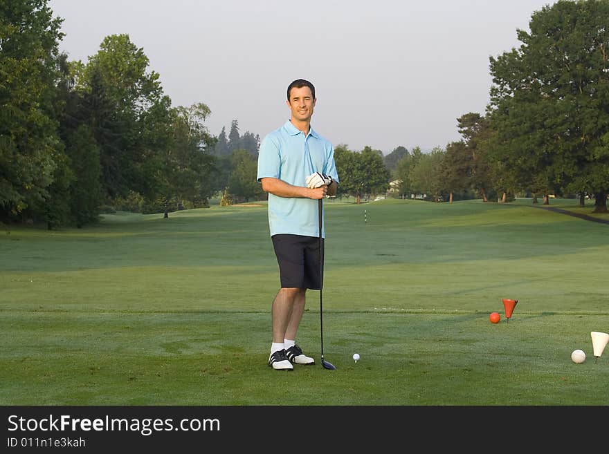 Male golfer casually standing on green holding golf club. Horizontal framed shot. Male golfer casually standing on green holding golf club. Horizontal framed shot.