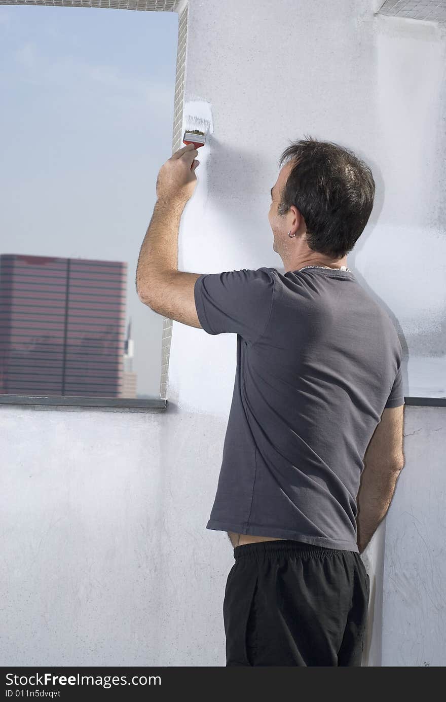 Man standing painting edge of wall next to window. Photo is taken from rear. Vertically framed shot. Man standing painting edge of wall next to window. Photo is taken from rear. Vertically framed shot.