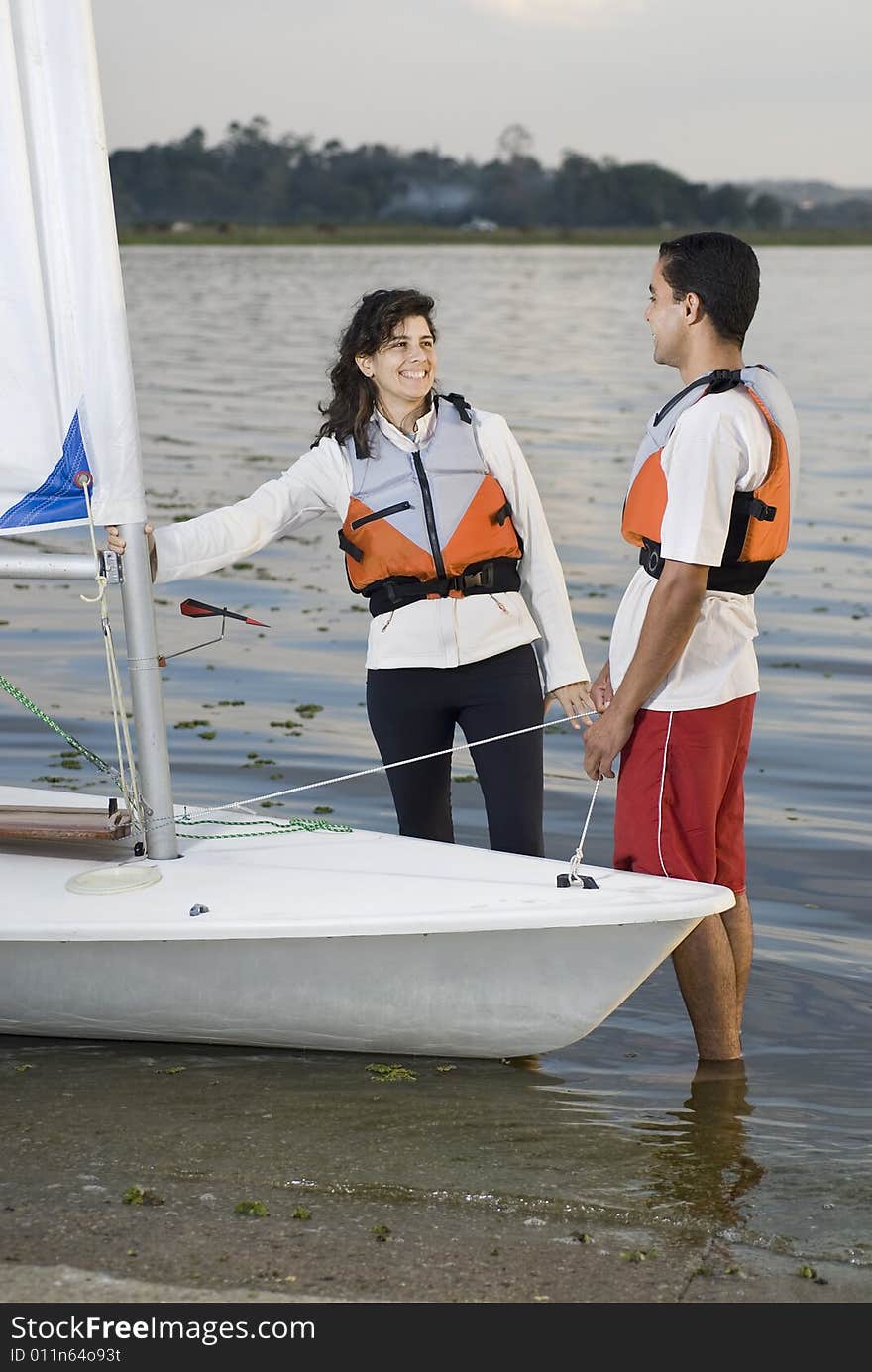 Smiling man and woman standing next to  sailboat looking at eachother. Vertically framed photo. Smiling man and woman standing next to  sailboat looking at eachother. Vertically framed photo