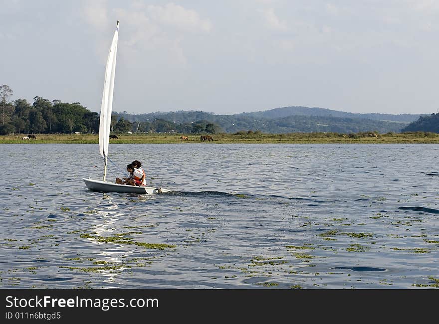 Couple sailing on sailboat in the distance. Sailing across lake. Horizontally framed photo. Couple sailing on sailboat in the distance. Sailing across lake. Horizontally framed photo