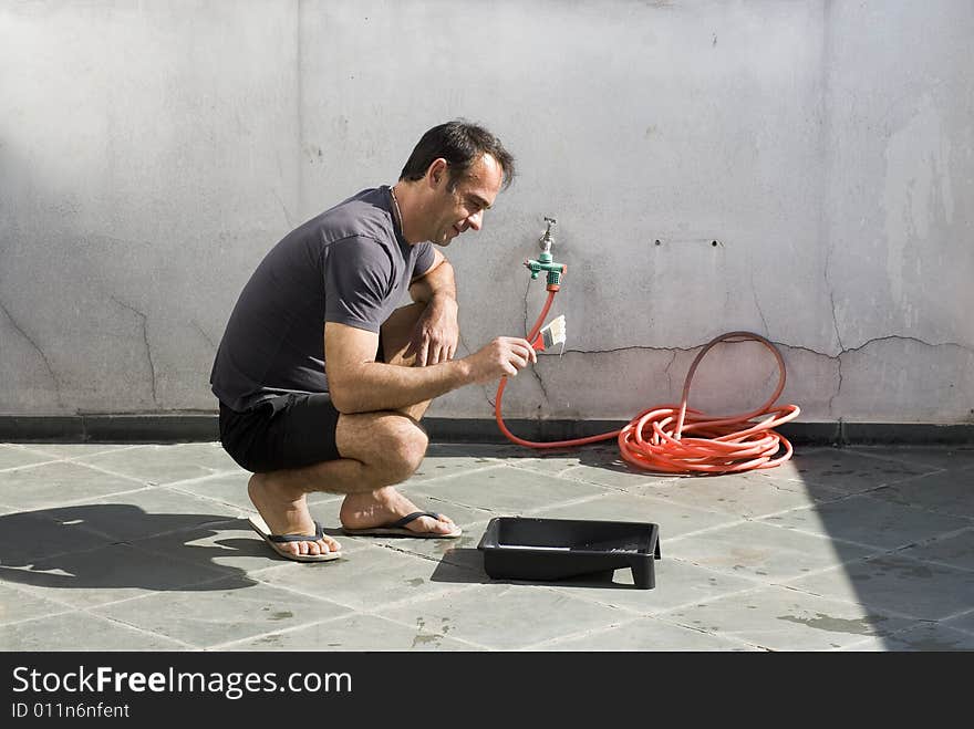 Man wearing sandals kneeling while looking at paint dripping off paintbrush. Horizontally framed shot. Man wearing sandals kneeling while looking at paint dripping off paintbrush. Horizontally framed shot.