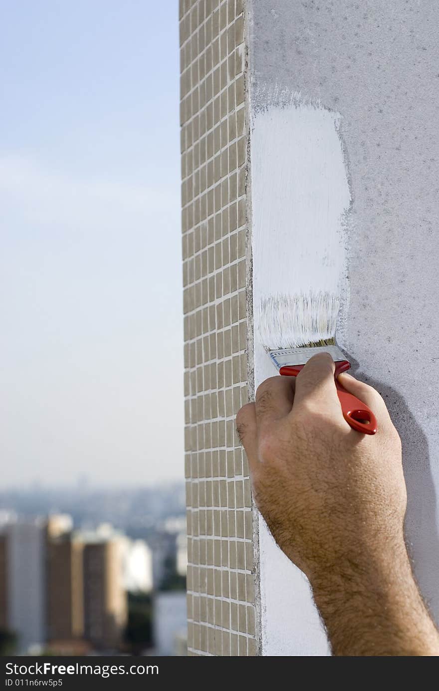 Closeup shot of a hand holding a paintbrush painting edge of a wall. Buildings in the background. Vertically framed shot. Closeup shot of a hand holding a paintbrush painting edge of a wall. Buildings in the background. Vertically framed shot.