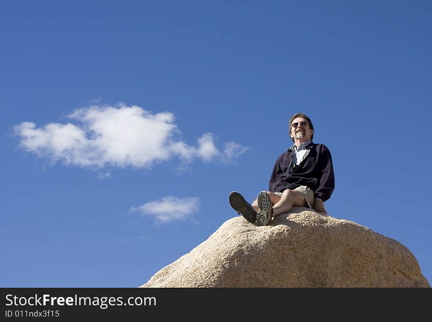 A hiker surveys his world while sitting on the top of a rock on a sunny day in Joshua Tree National Park. A hiker surveys his world while sitting on the top of a rock on a sunny day in Joshua Tree National Park.