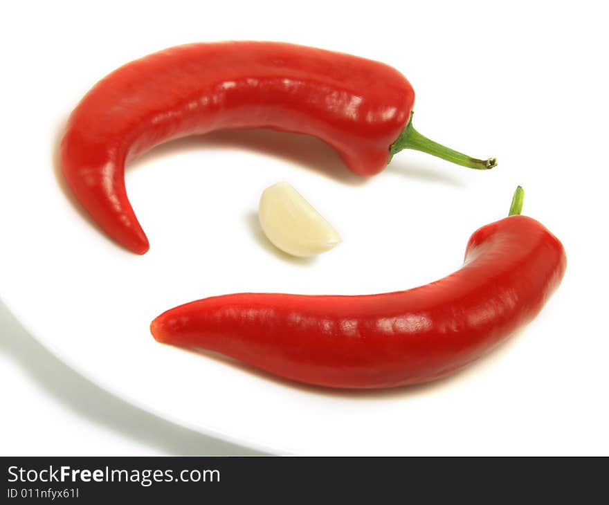 Two fresh chili peppers and a skinless clove of garlic on a white plate and isolated on white background. Two fresh chili peppers and a skinless clove of garlic on a white plate and isolated on white background