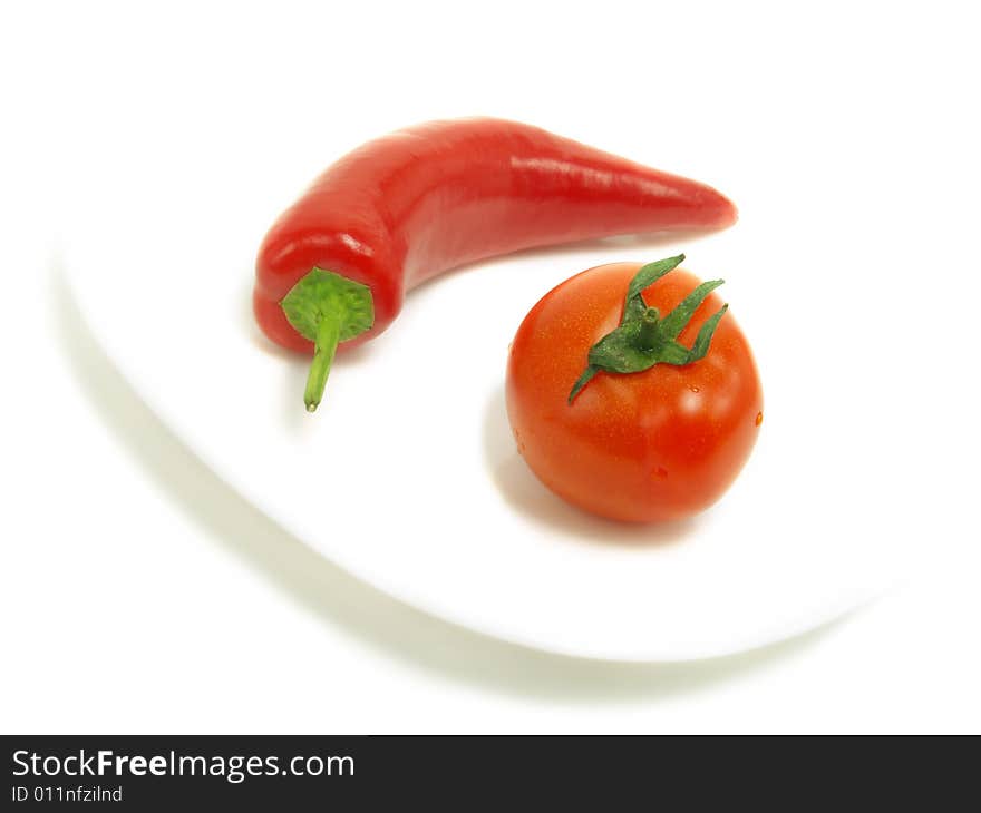 A fresh tomato and a ripe chili pepper on a white plate and isolated on white background. A fresh tomato and a ripe chili pepper on a white plate and isolated on white background