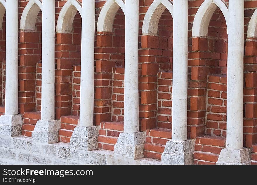 A row of stone columns against red brick wall. Tsaritsino park in Moscow.