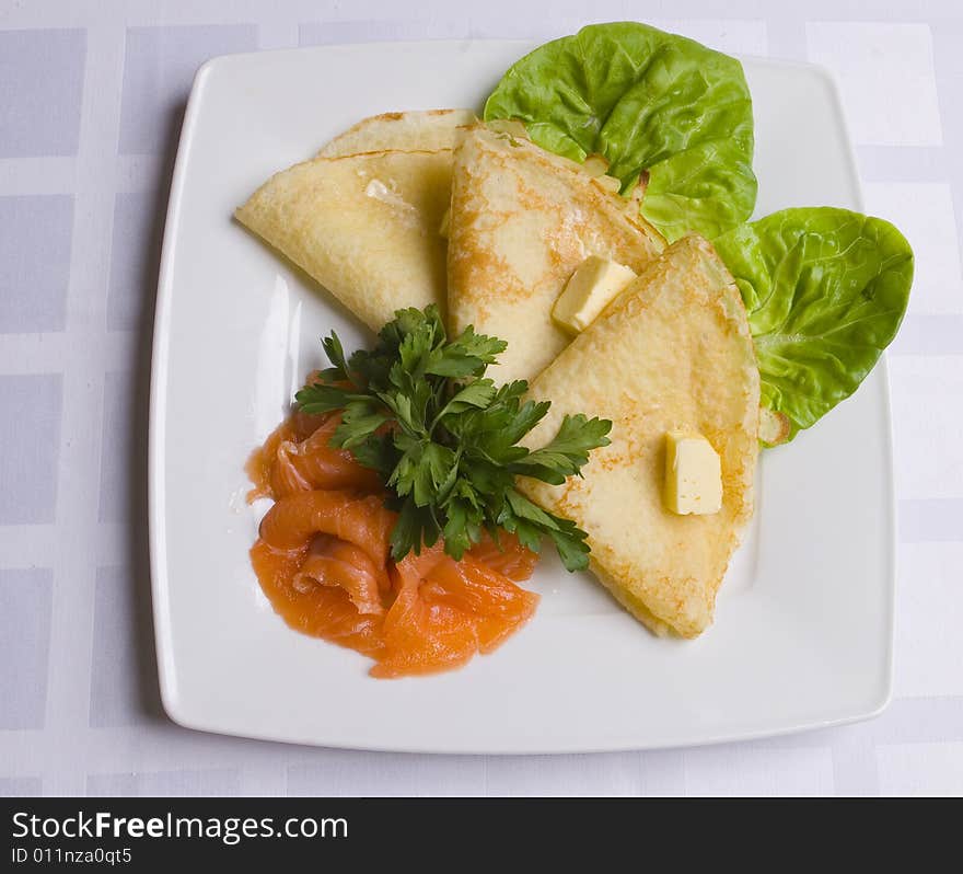 Pancakes with salty salmon on white plate on white ground