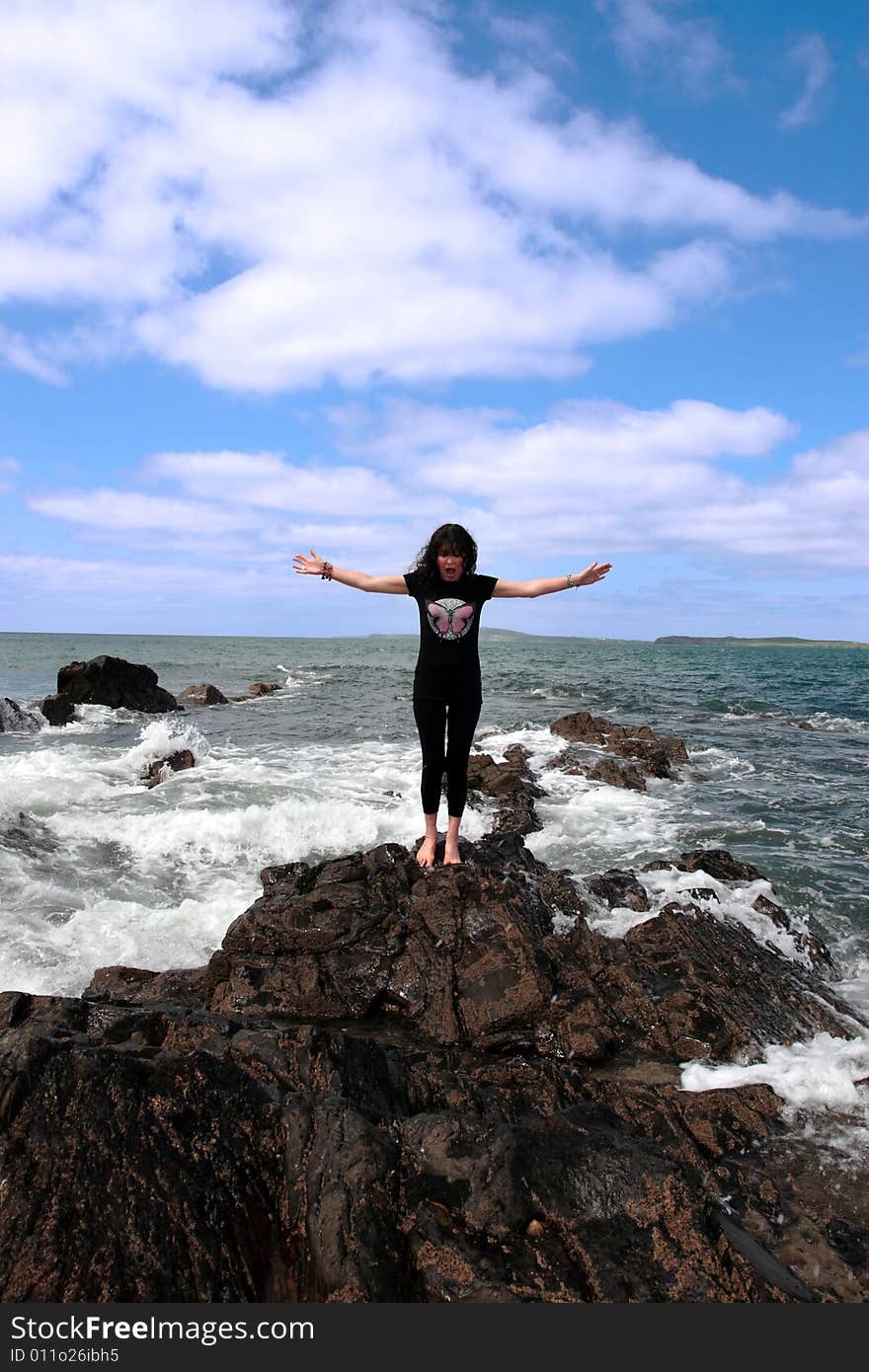 A beautiful woman doing yoga on the edge of the rocks with waves splashing to show a healthy way to live a happy and relaxed lifestyle in a world full of stress. A beautiful woman doing yoga on the edge of the rocks with waves splashing to show a healthy way to live a happy and relaxed lifestyle in a world full of stress